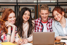 Four GED students working together at a laptop, smiling and collaborating in a supportive learning environment at Stella Edu-Centre